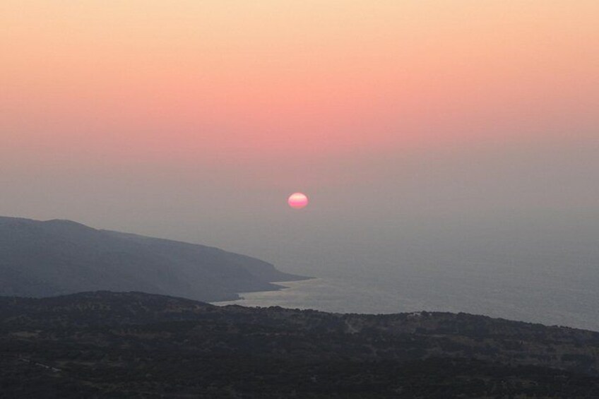 A sunset over a coastal landscape with hills in the foreground and a body of water in the middle ground. 2
