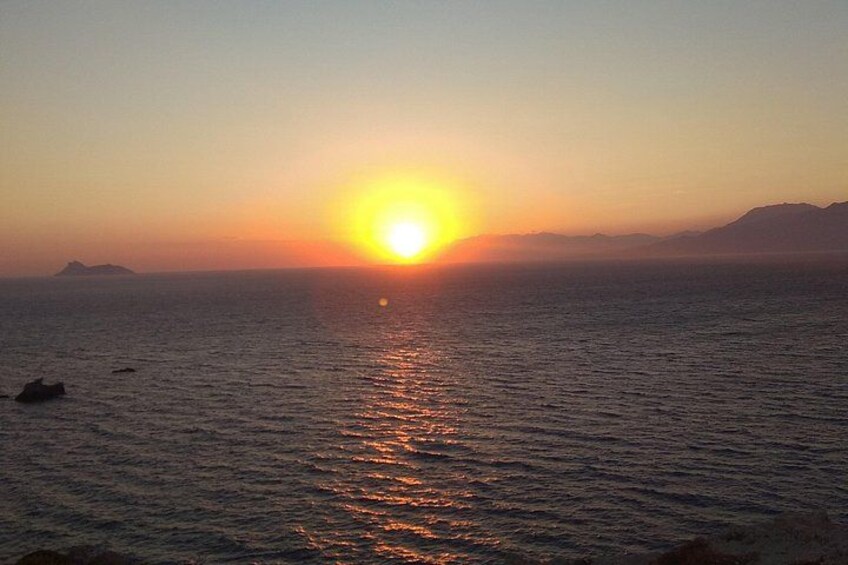 A sunset over a calm sea with a visible horizon and distant landforms. 5