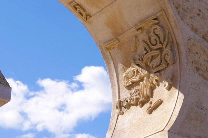 Une arche en pierre ornée de sculptures complexes, et un ciel bleu clair parsemé de nuages. 2