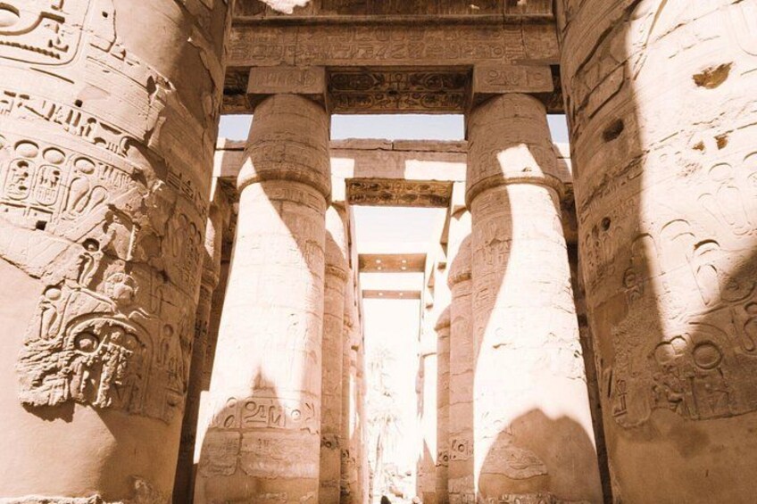 Forntida egyptiska kolonner med hieroglyfer, en stenstruktur och en skugga av en person. 5