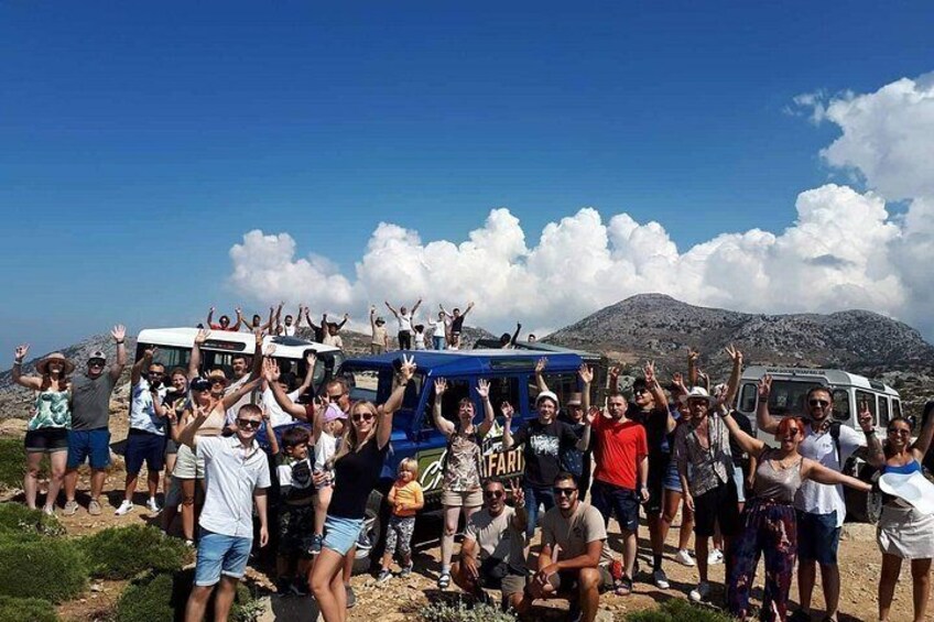 En gruppe mennesker juber med armene i vejret, en blå bil og et bjergrigt landskab i baggrunden. 1