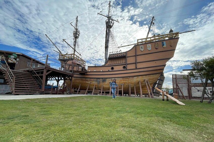 A large wooden ship under construction with scaffolding and a grassy area in the foreground. 2