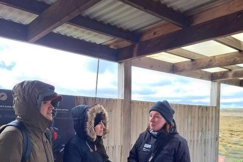 Three people standing in a covered outdoor area with a wooden structure and a view of the landscape. 3