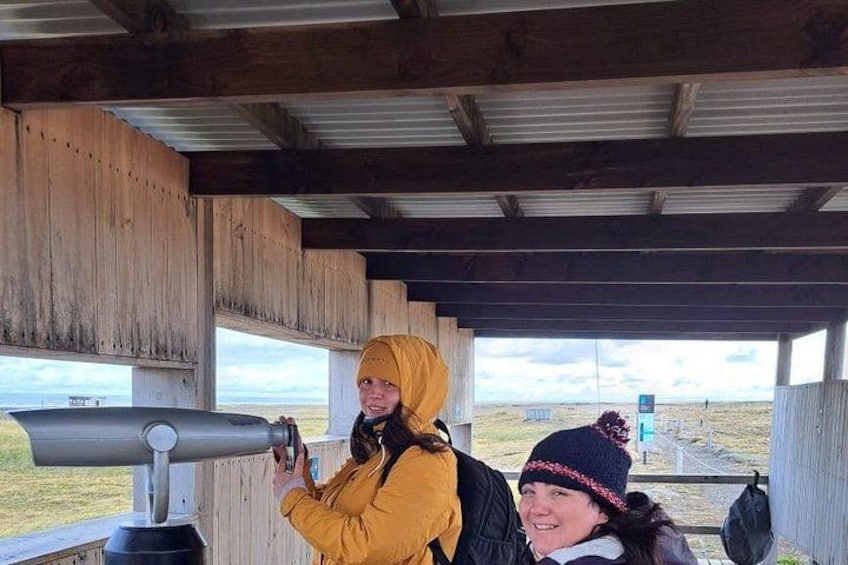 Two people using a telescope under a wooden shelter with a view of a grassy landscape. 4