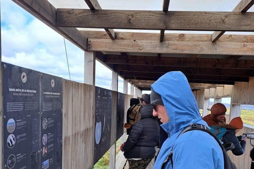 A wooden structure with informational signs, a person in a blue jacket, and another in a black jacket. 2