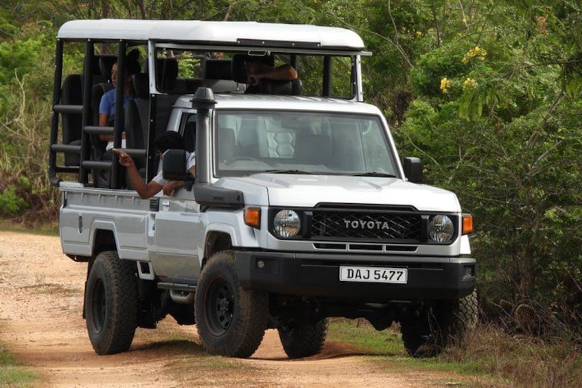 A white Toyota off-road vehicle with a raised suspension, driving on a dirt road surrounded by greenery. 1