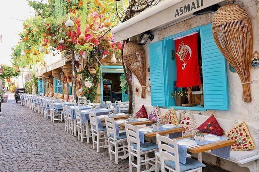 Outdoor dining tables with blue chairs, a cobblestone street, and a building with blue shutters and a red flag. 2
