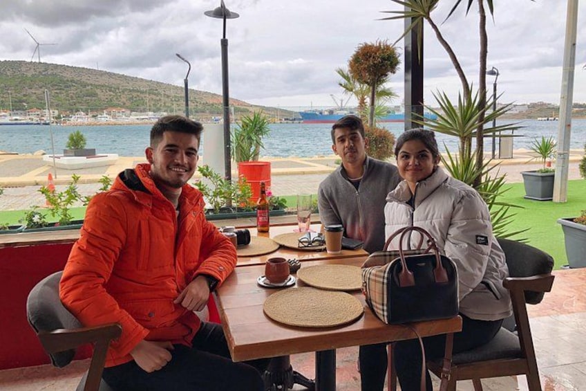 Three people seated at an outdoor table with a view of the sea and hills in the background. 5