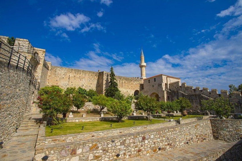 A historic stone fortress with a minaret, lush green trees, and a clear blue sky. 3