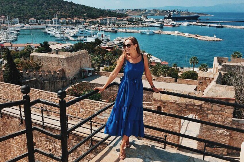 A woman in a blue dress standing on a stone staircase overlooking a harbor with boats and a ship. 3