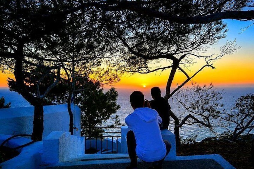 Un coucher de soleil sur la mer, avec les silhouettes de personnes et d’arbres. 2