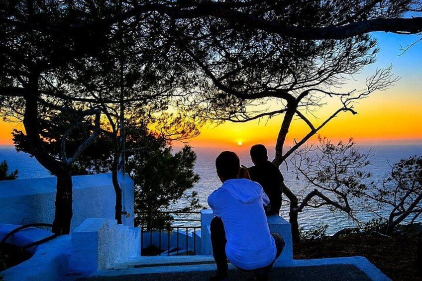 A sunset over the sea with silhouettes of people and trees. 2