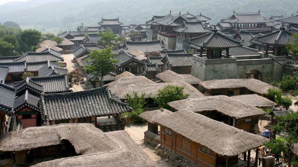 Traditional buildings at a Korean Folk Village nestled beside forested hills hand mountains