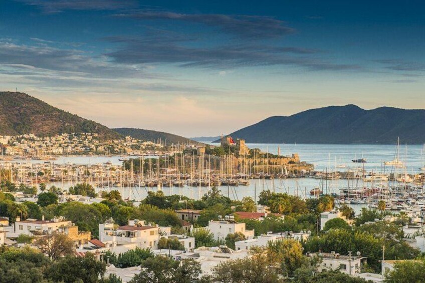 A coastal town with a marina, buildings, and hills in the background. 2