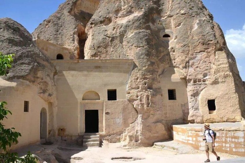 A rock-cut structure with a doorway, steps leading up to it, and a person standing in front. 4