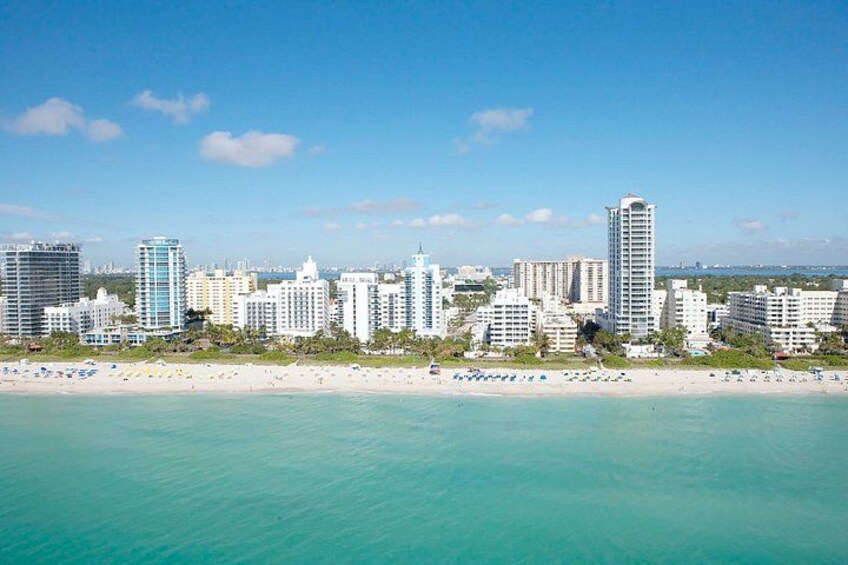 A coastal cityscape with a beach, high-rise buildings, and clear turquoise waters. 3