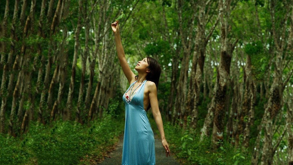 Woman in a blue dress holding a leaf and surrounded by trees in Sekinchan 1