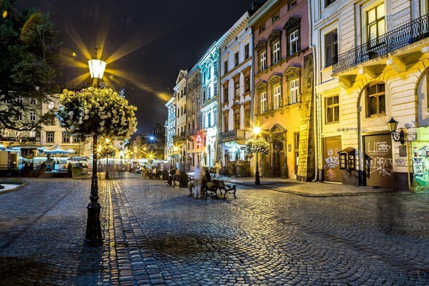 A cobblestone street at night with illuminated buildings and a street lamp. 3
