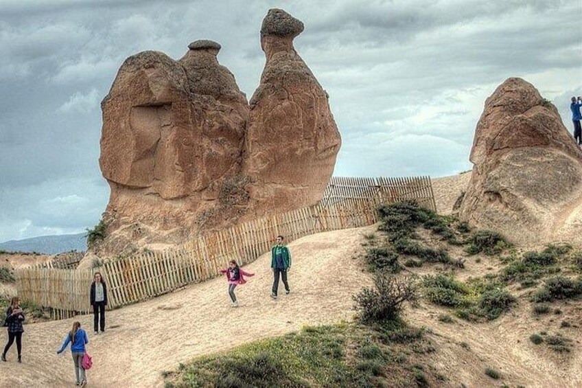 A sandy trail with large rock formations, a wooden fence, and people walking. 2