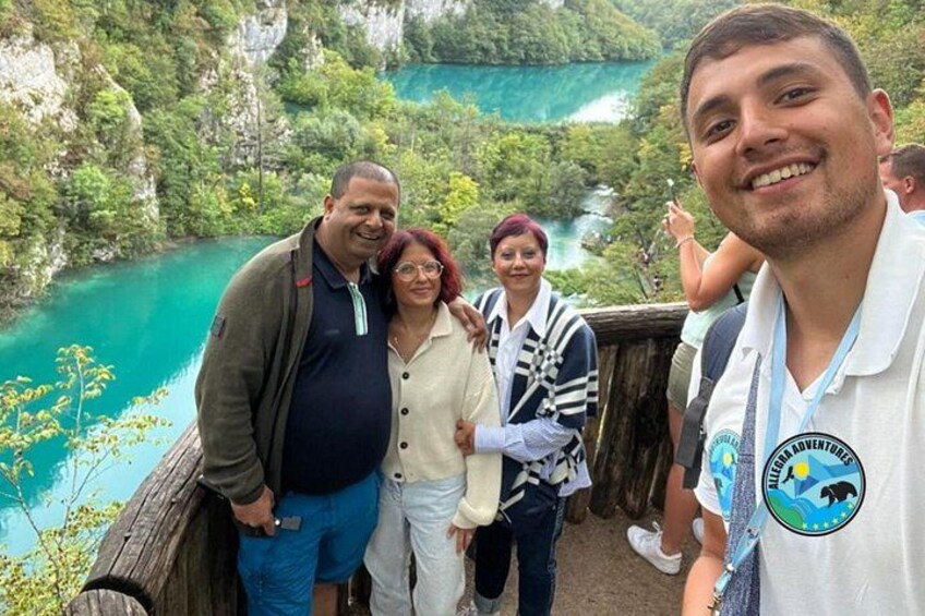 Un grupo de personas de pie sobre una plataforma de madera, con vistas a un lago turquesa rodeado de vegetación. 2