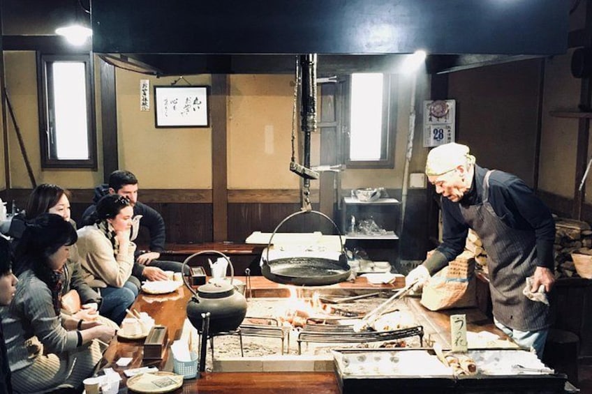 A chef preparing food in a traditional kitchen with diners watching. 1