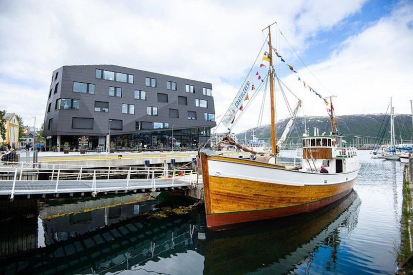 Un bateau en bois était amarré à un quai, avec un bâtiment moderne en arrière-plan. 1