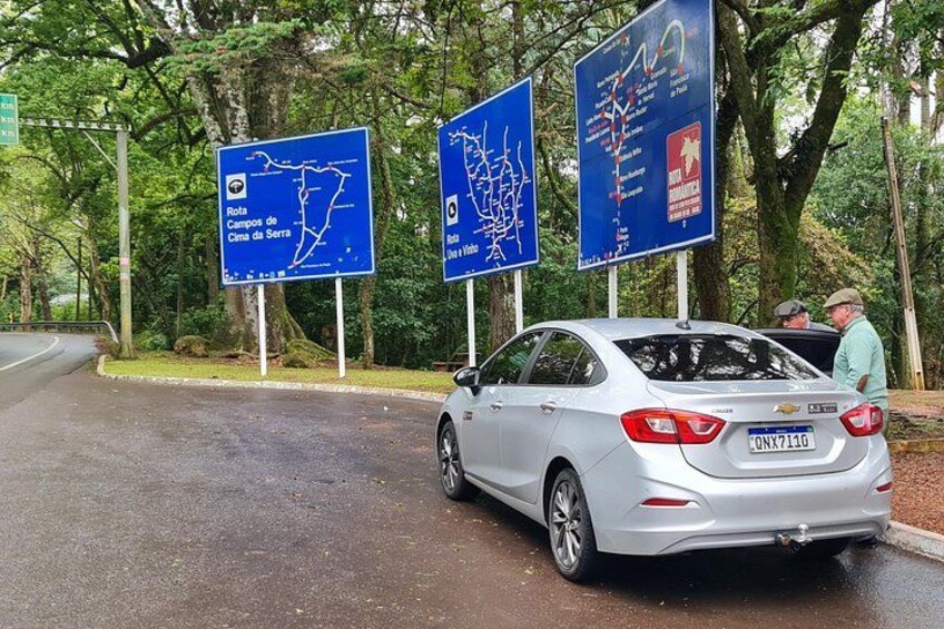 Un coche plateado estacionado en una carretera mojada con tres señales direccionales azules al fondo. 5