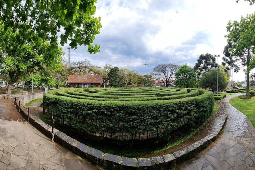 Un jardín ajardinado con un laberinto, un camino de piedra y un edificio al fondo. 3