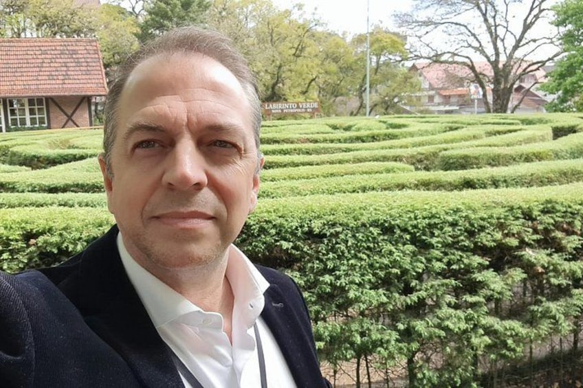 Un hombre con traje se toma un selfie con un laberinto de setos al fondo. 4