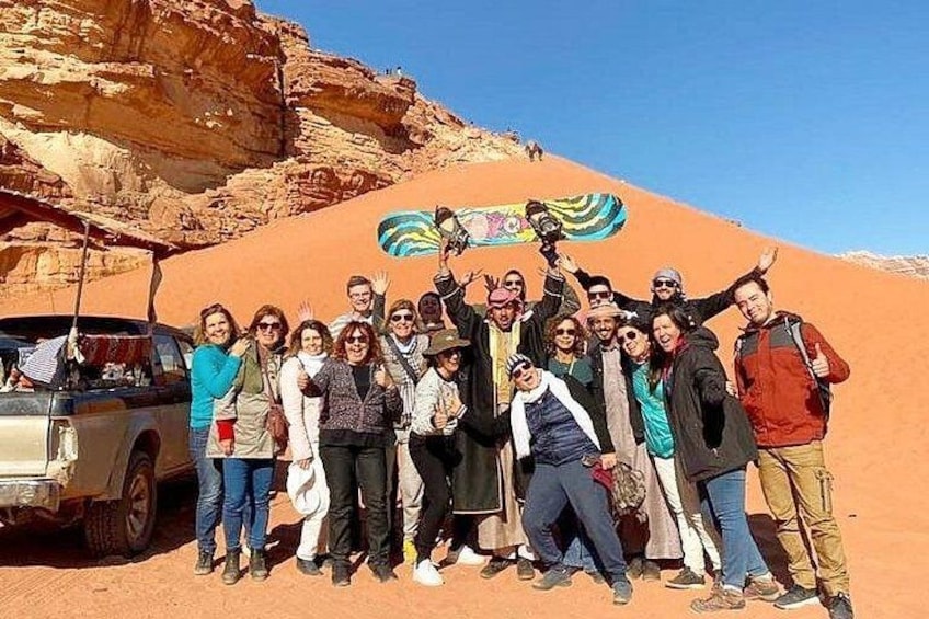Un groupe de personnes posant dans un désert, avec une dune en arrière-plan et un véhicule garé à proximité. 4