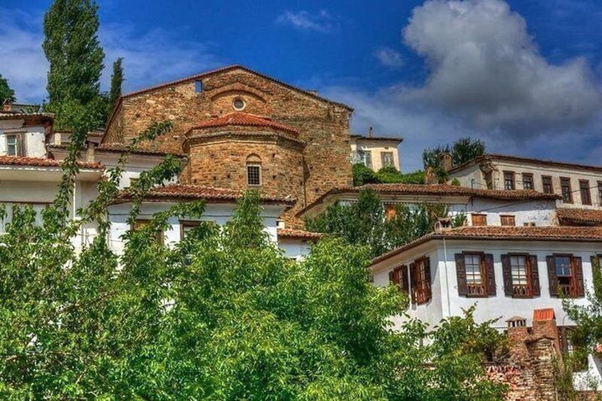A historic stone building with a red-tiled roof, surrounded by lush greenery and white buildings with wooden shutters. 5