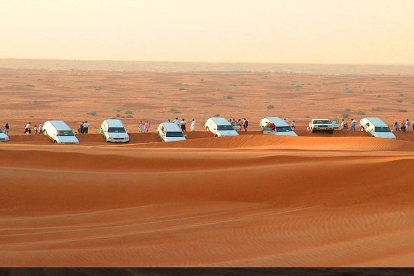 A desert landscape with white vehicles parked on dunes, surrounded by people. 3