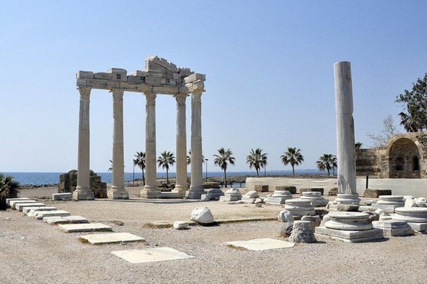 Ancient ruins with columns and a tall pillar, palm trees, and a clear sky. 2