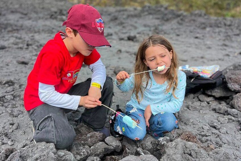 Two children sitting on a rocky surface, one holding a stick. 1
