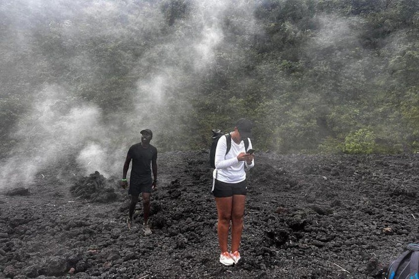 Two people standing on a volcanic terrain with steam rising from the ground. 5