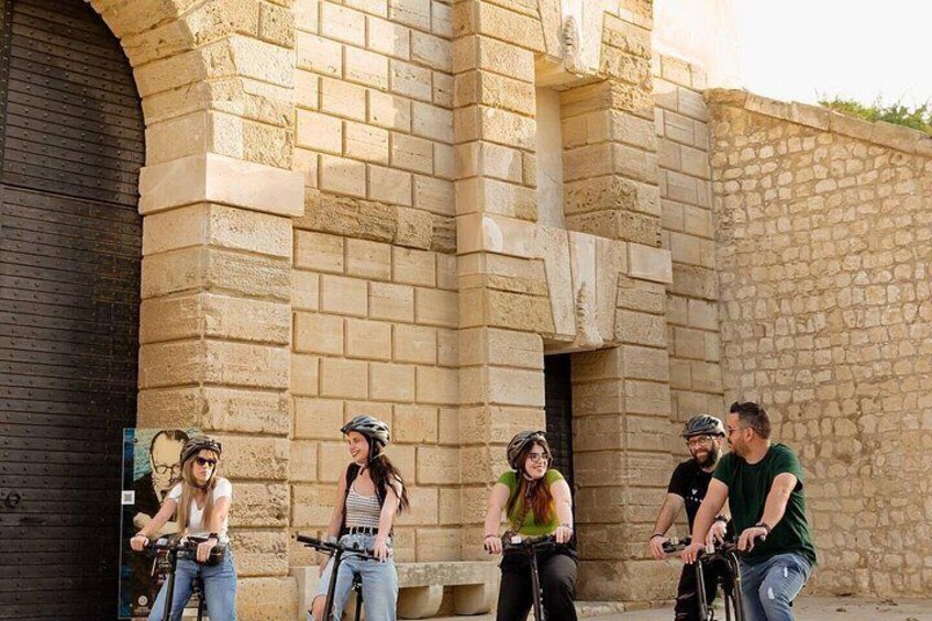 A group of people on bicycles in front of a stone building with an arched doorway. 4
