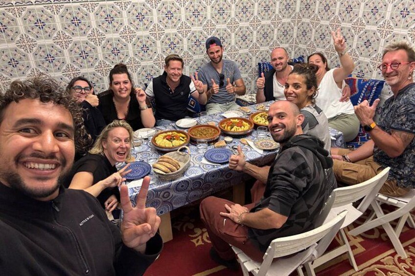 Un groupe de personnes est assis autour d’une table où se trouve de la nourriture, dans une pièce dont les murs sont recouverts de carreaux décoratifs. 4