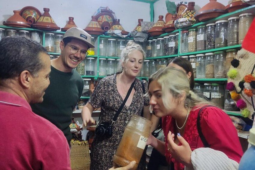 Un groupe de personnes se trouve dans un marché où l’on peut voir des étagères remplies de poteries et de bocaux. 1