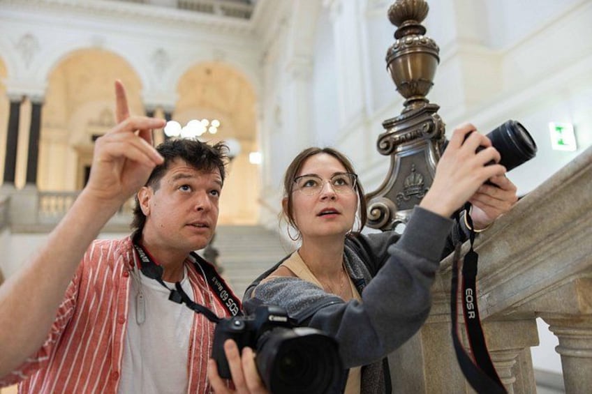 Two people taking a photo with a camera in a historical building with arches and columns. 5