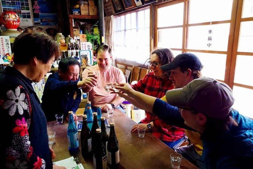 A group of people sitting around a wooden table with bottles and glasses, in a room with wooden walls and windows. 1