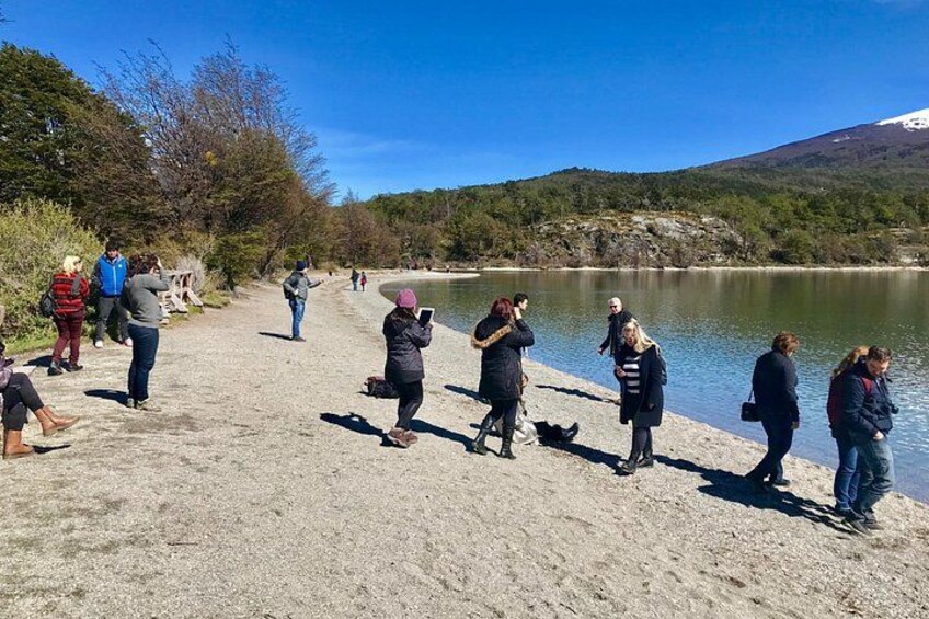 Personas de pie junto a un lago, algunas tomando fotografías, con árboles y colinas al fondo. 4