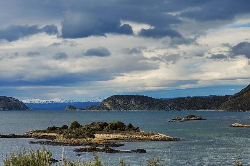 Un lago con islas rocosas, cielo nublado y montañas a lo lejos. 3