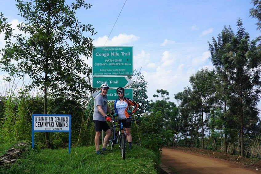 A trail sign, a dirt path, and cyclists. 1