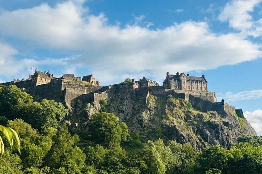 A historic castle on a hill with dense greenery and a clear sky. 1