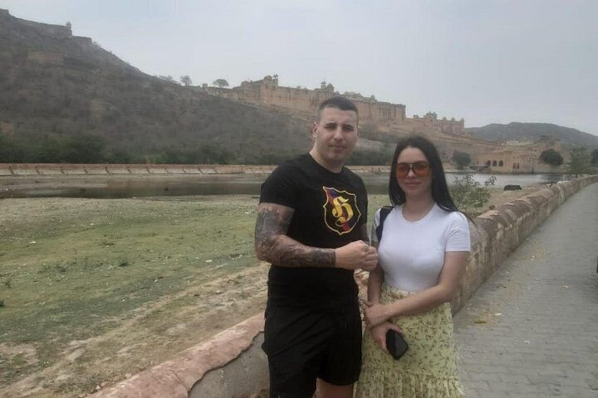 A man and a woman standing by a historical site with a river and fortifications in the background. 2