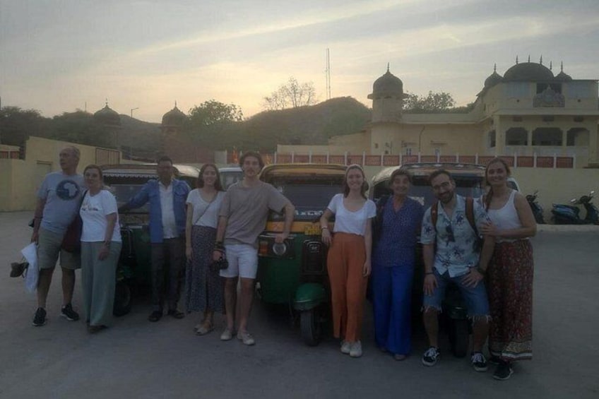 A group of people standing in a line with a tuk-tuk and a building in the background. 3