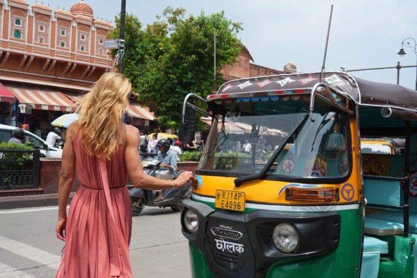 A woman in a pink dress interacting with a green and yellow auto-rickshaw on a busy street. 4