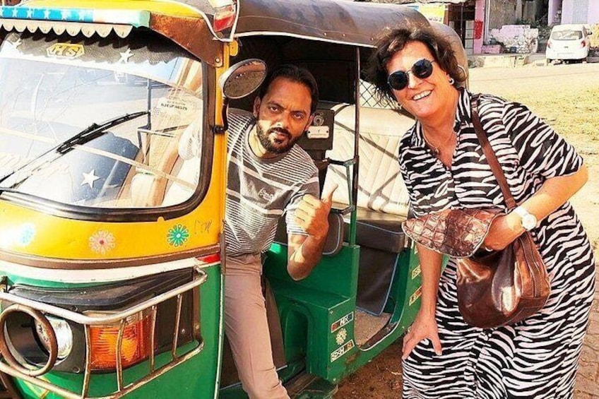 A yellow auto-rickshaw with a green seat, a person sitting inside, and another person standing outside. 1
