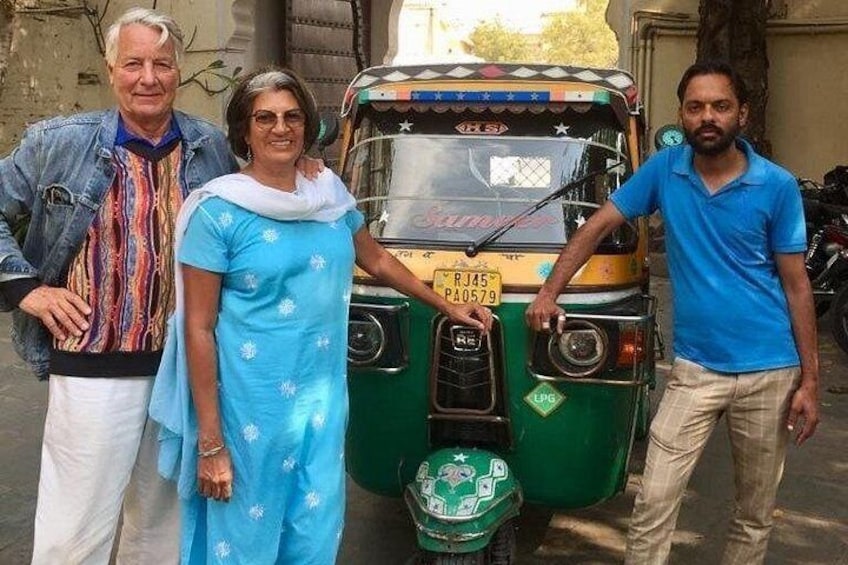A green auto-rickshaw parked on a street with three people standing beside it. 4