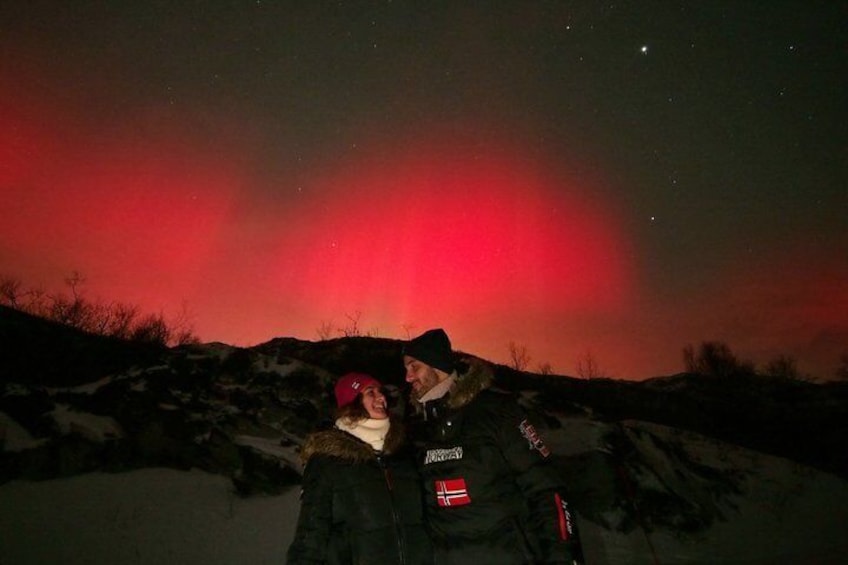 Zwei Personen stehen auf einem verschneiten Hügel, am Himmel ein rotes Polarlicht. 4